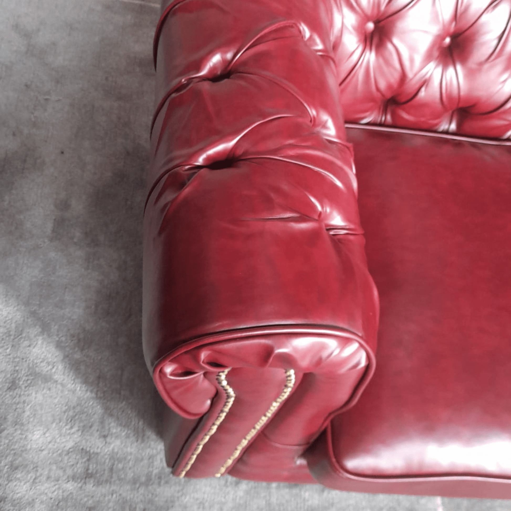 Close-up of a red leather couch with tufted backrest on a gray floor.