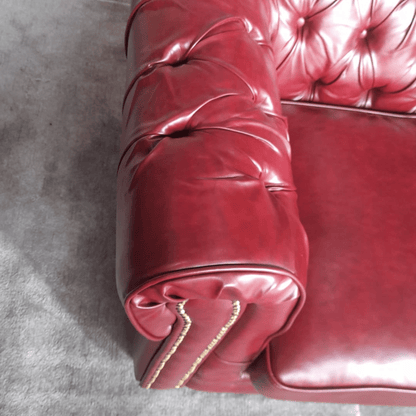 Close-up of a red leather couch with tufted backrest on a gray floor.