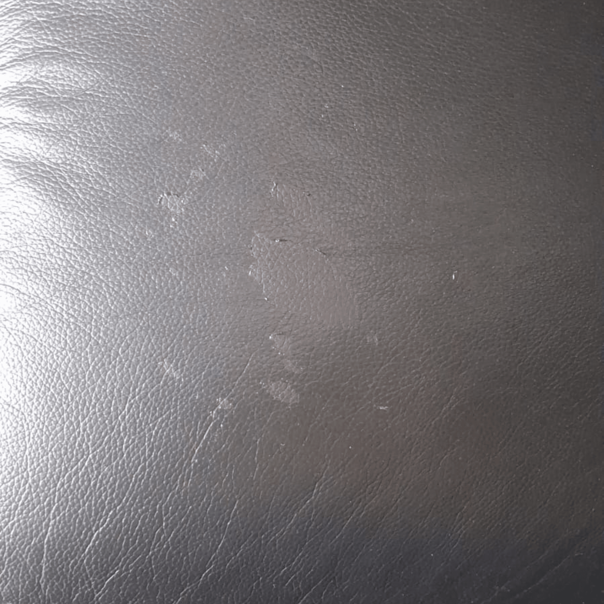 A close-up of a dark gray textured material, resembling leather or faux leather, with visible scuffs and scratches.