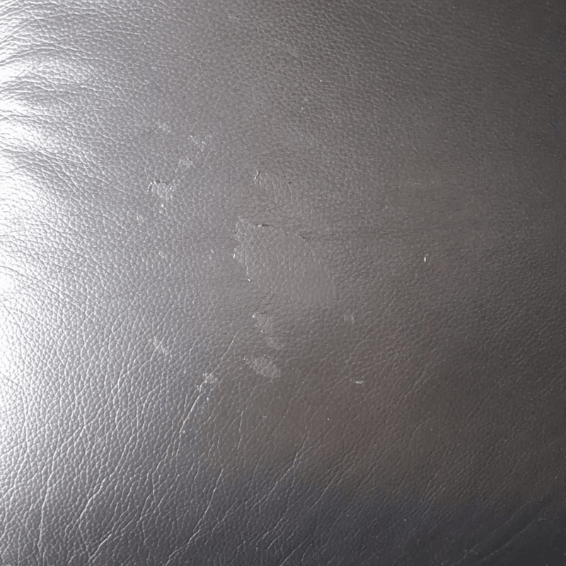 A close-up of a dark gray textured material, resembling leather or faux leather, with visible scuffs and scratches.