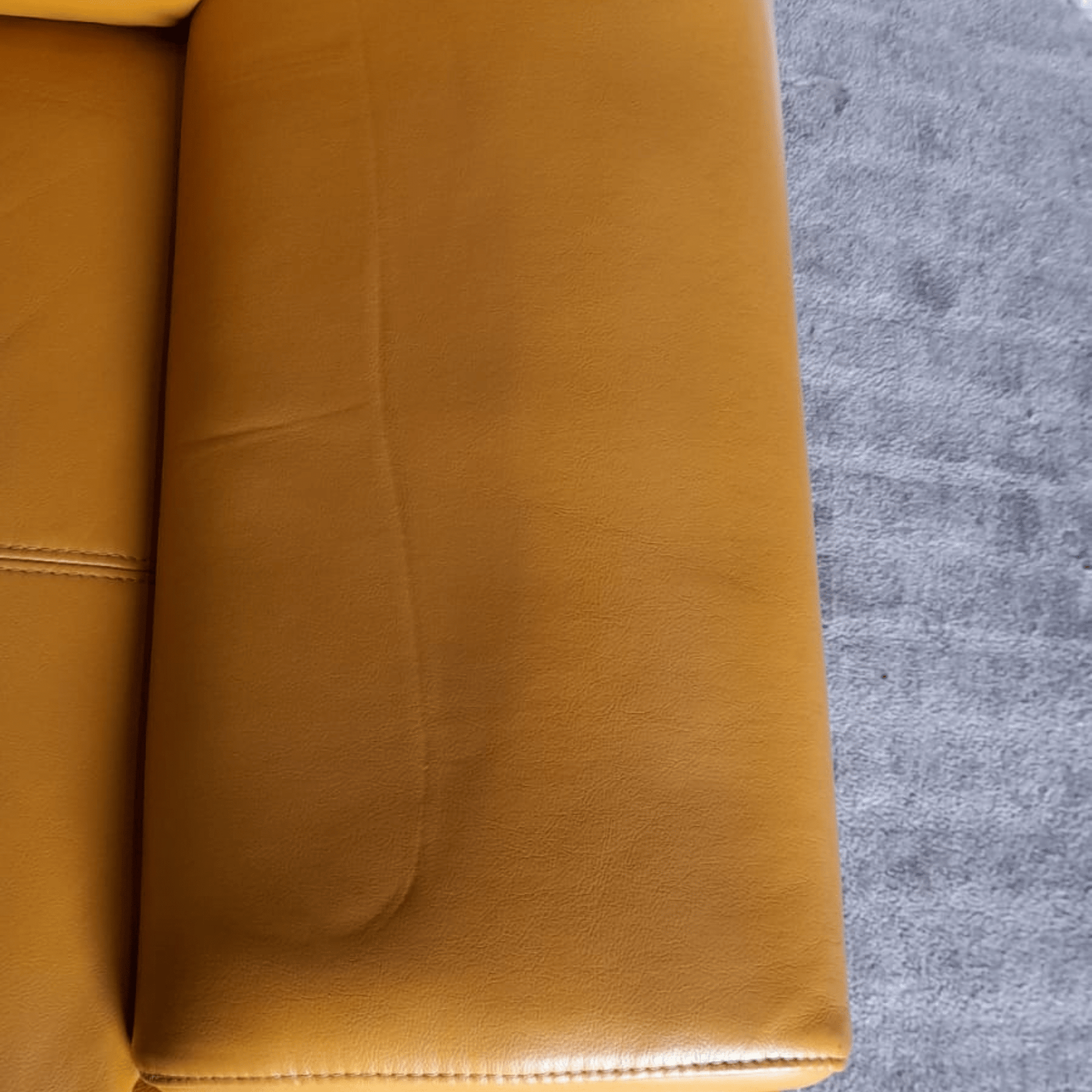 Close-up of a yellow leather couch corner on a gray carpet