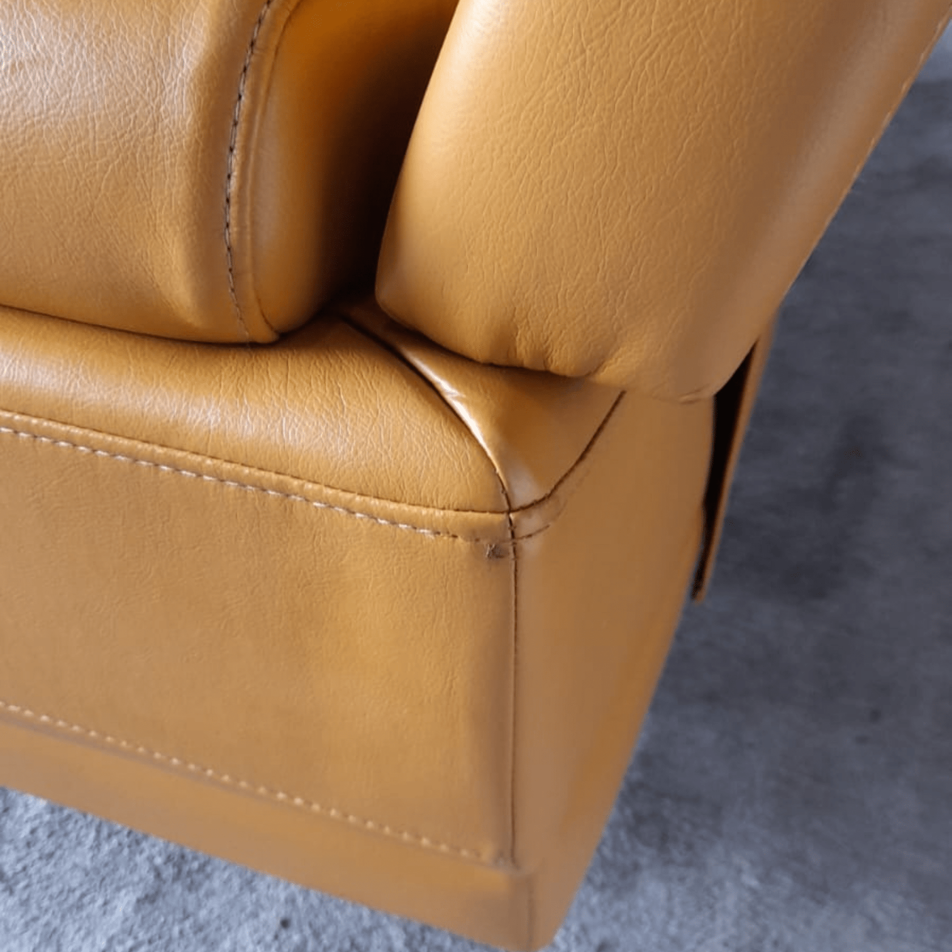 Close-up of a yellow leather armchair corner on a gray floor.