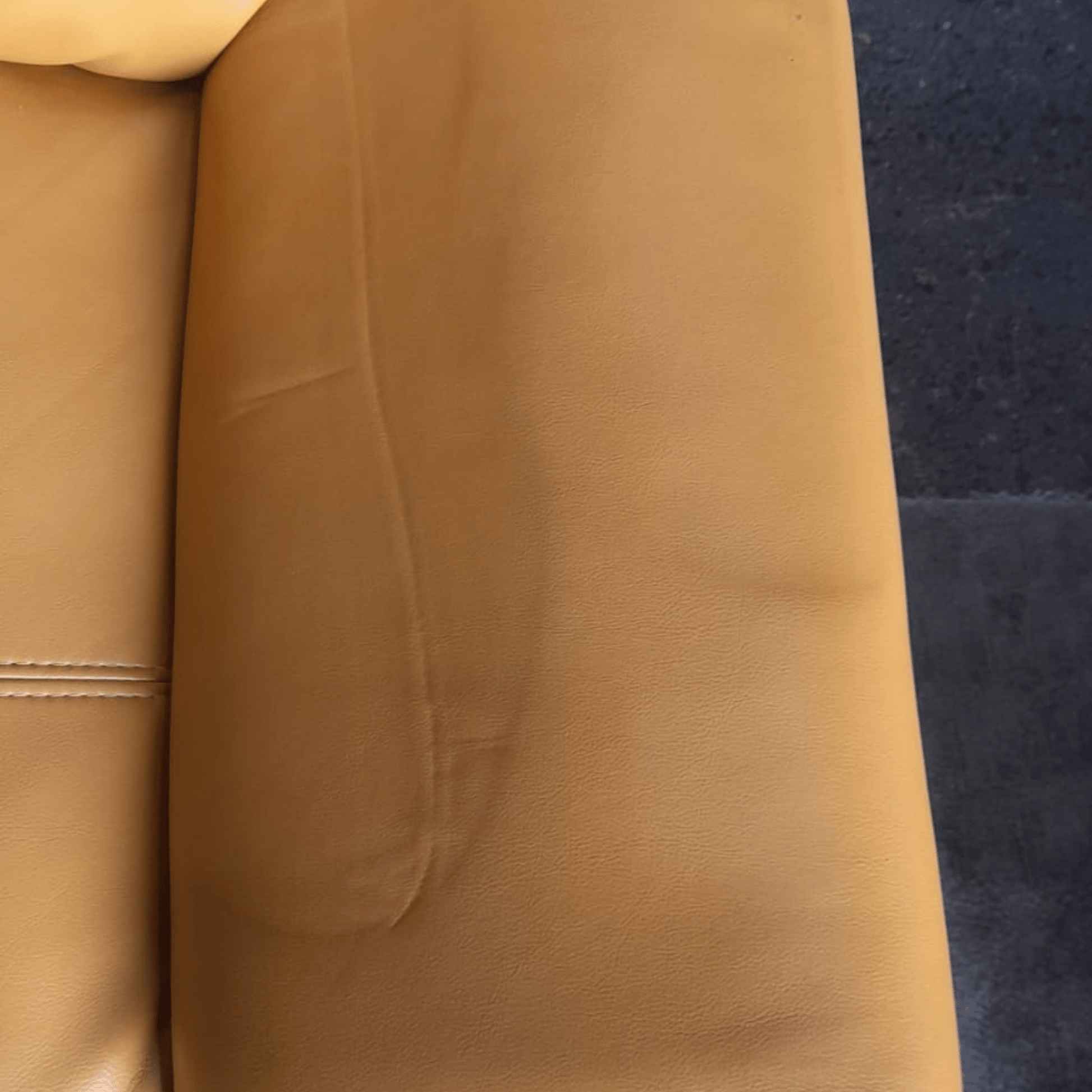 Close-up of a brown leather couch with a dark blue carpet background