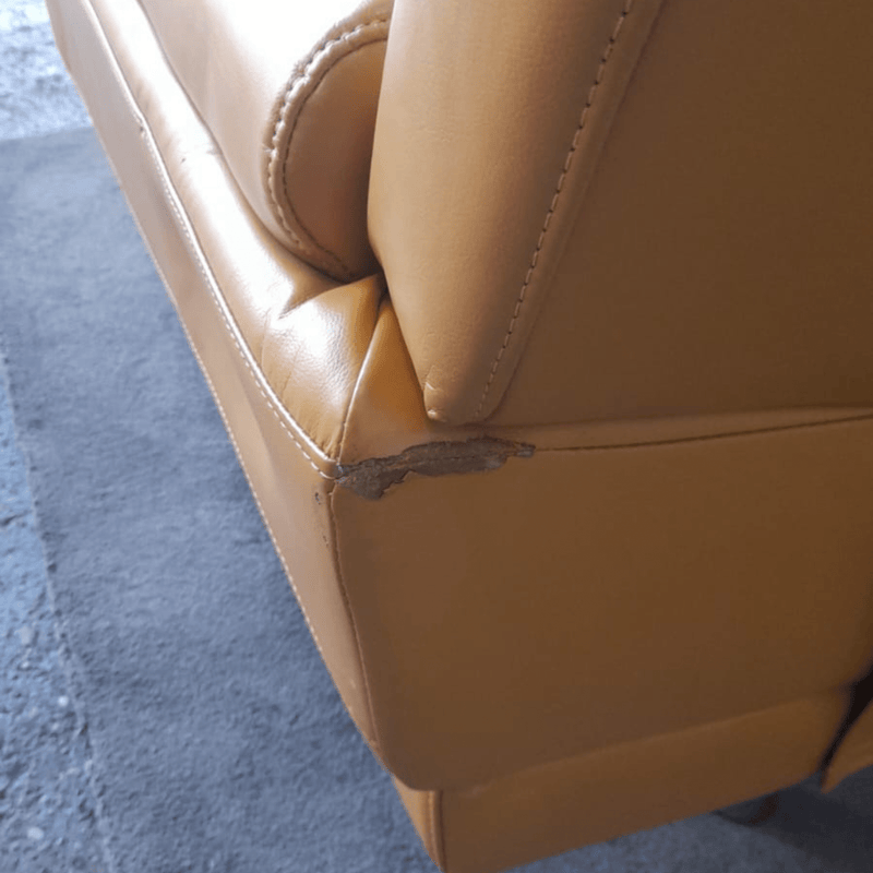 Close-up of a brown leather chair with a visible tear on a blue carpet.
