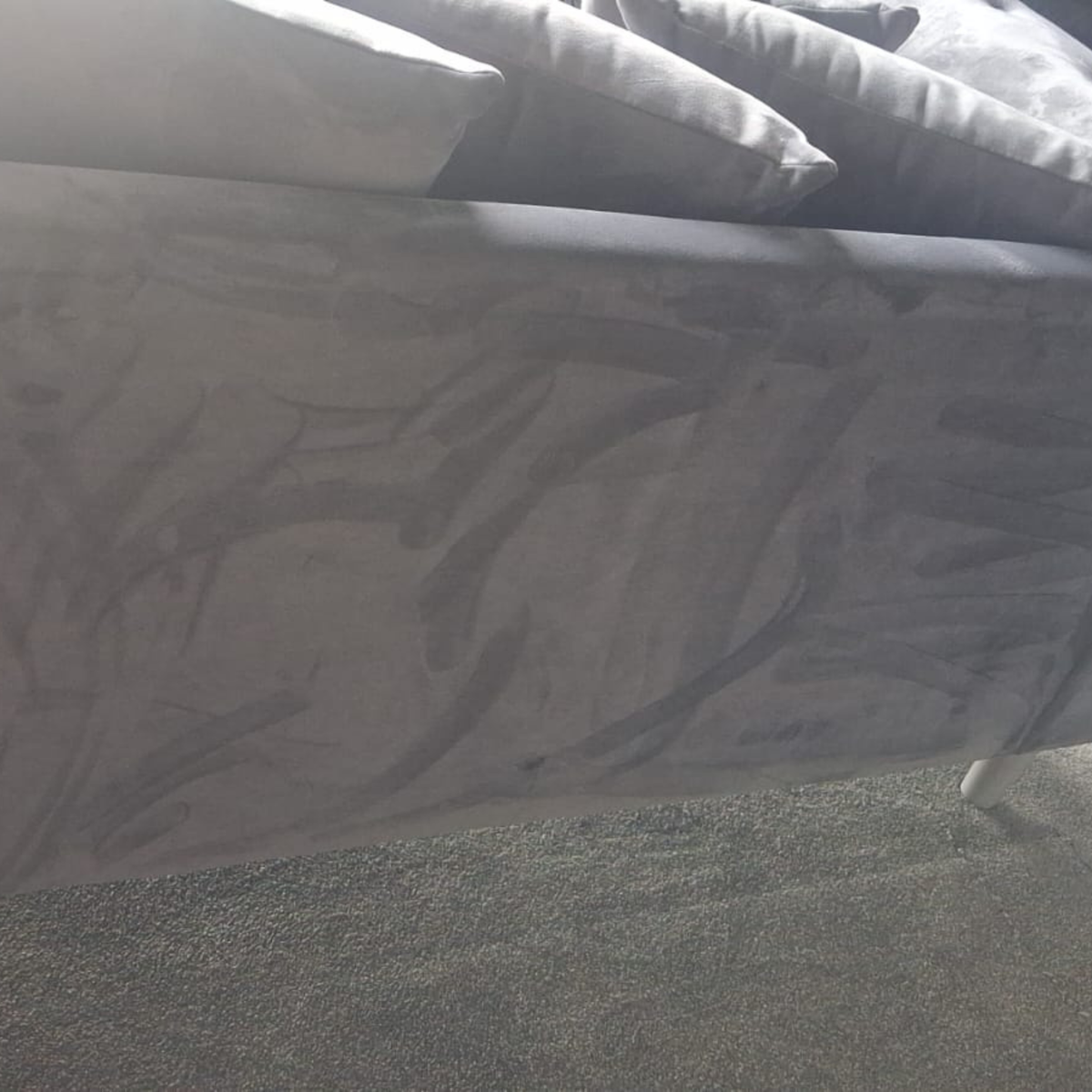 A close-up view of a gray upholstered bed frame with patterned gray bedding and pillows, resting on a gray carpeted floor.