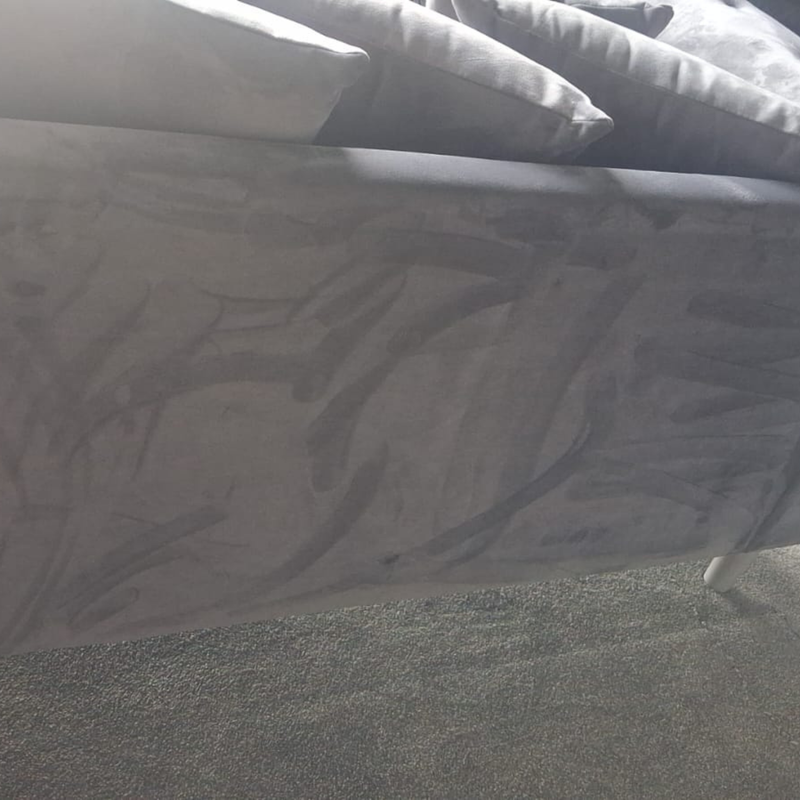 A close-up view of a gray upholstered bed frame with patterned gray bedding and pillows, resting on a gray carpeted floor.
