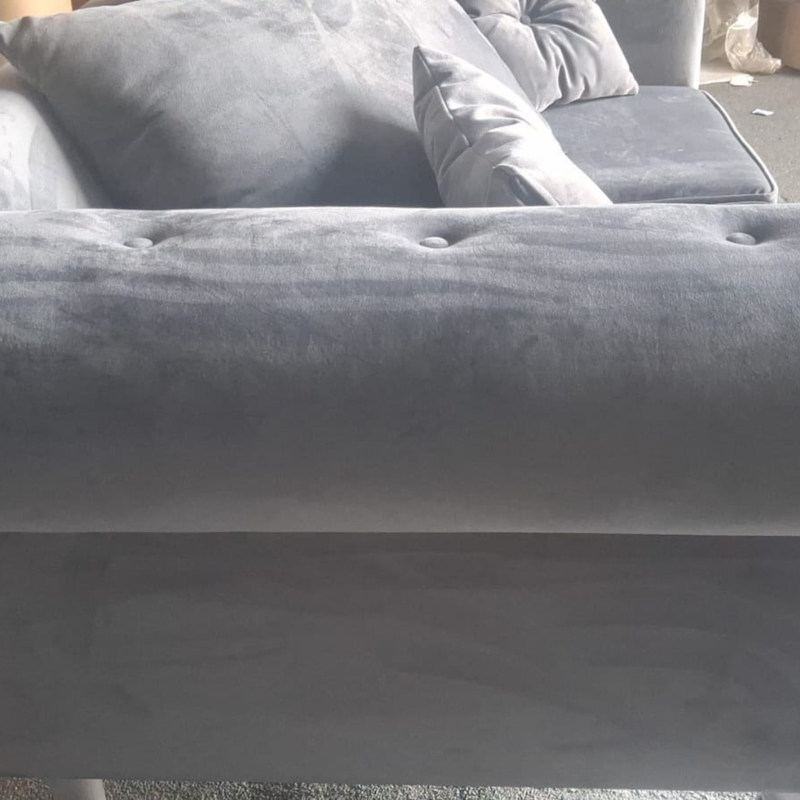Close-up of a gray velvet tufted sofa armrest with matching cushions in a real indoor setting.