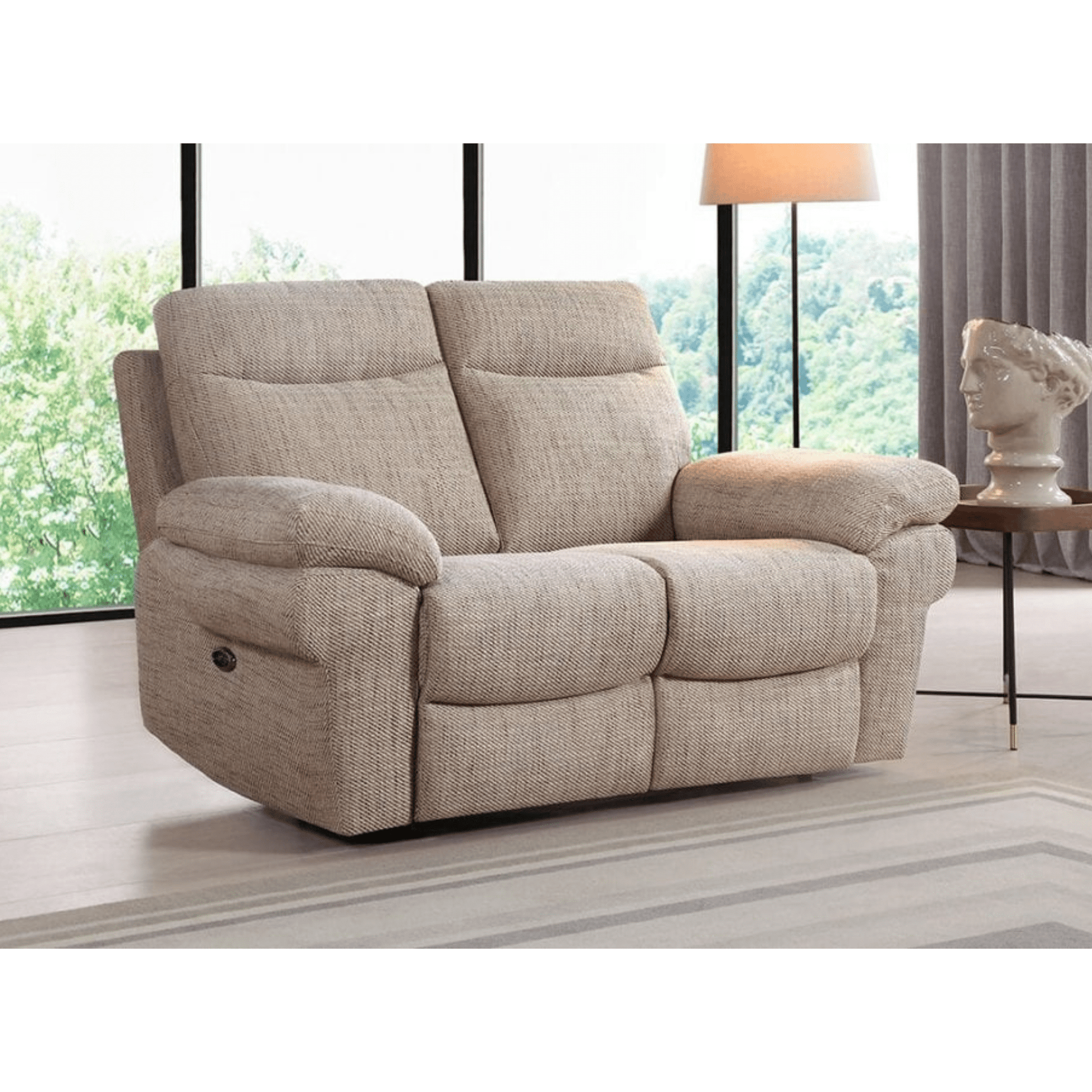 Beige recliner sofa in a living room setting with large windows and a lamp.