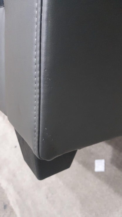 Close-up of a black leather armchair corner on a light gray surface.