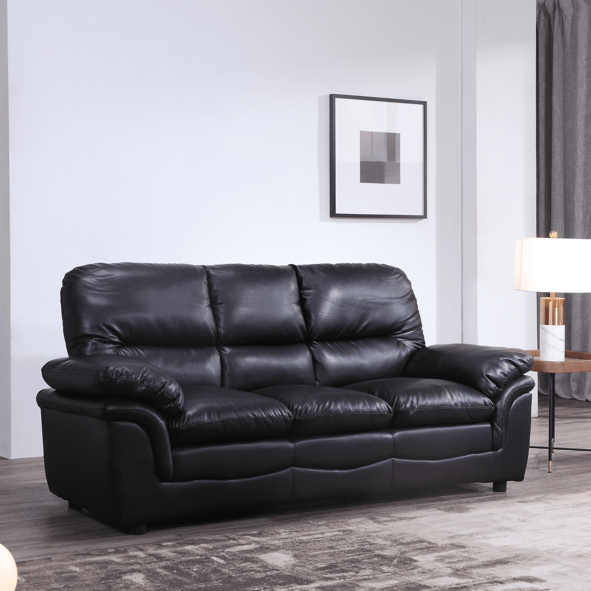 Black leather sofa in a living room setting with a lamp and framed picture on the wall.