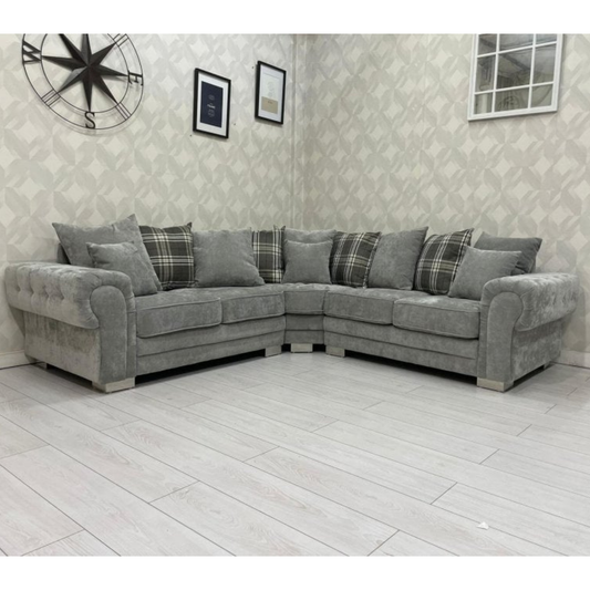 Gray sectional sofa with plaid cushions in a room with patterned wallpaper and a clock.