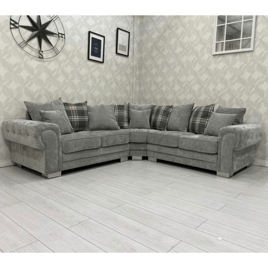 Gray sectional sofa with plaid cushions in a room with patterned wallpaper and a clock.