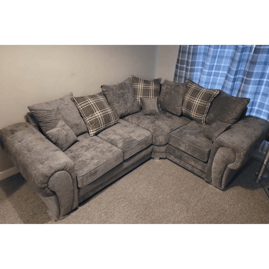Gray sectional sofa with plaid cushions in a room with a blue curtain.