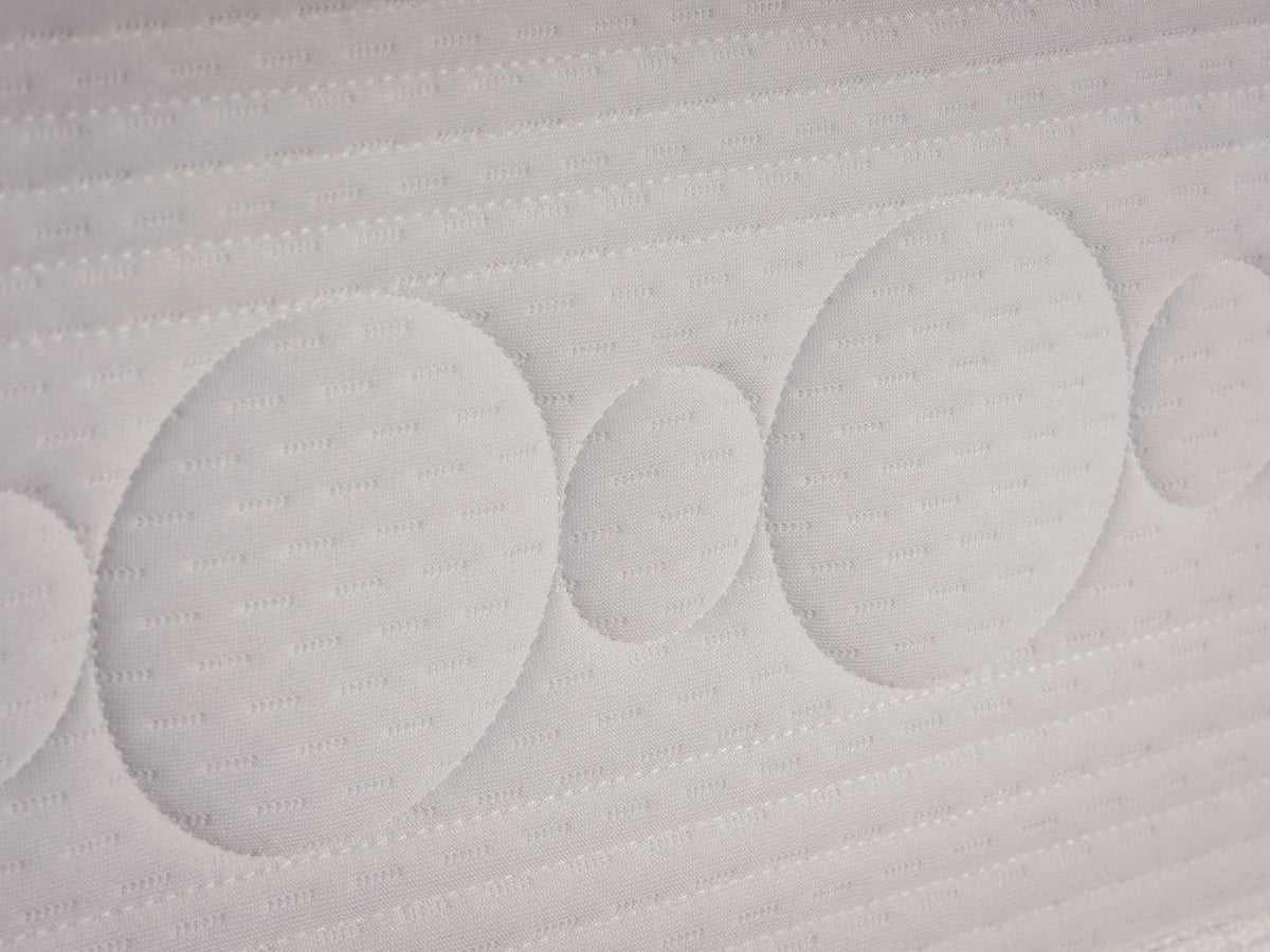 Close-up of a white quilted mattress or sofa cushion with circular tufted patterns and stitched horizontal channels.