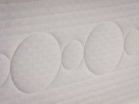 Close-up of a white quilted mattress or sofa cushion with circular tufted patterns and stitched horizontal channels.